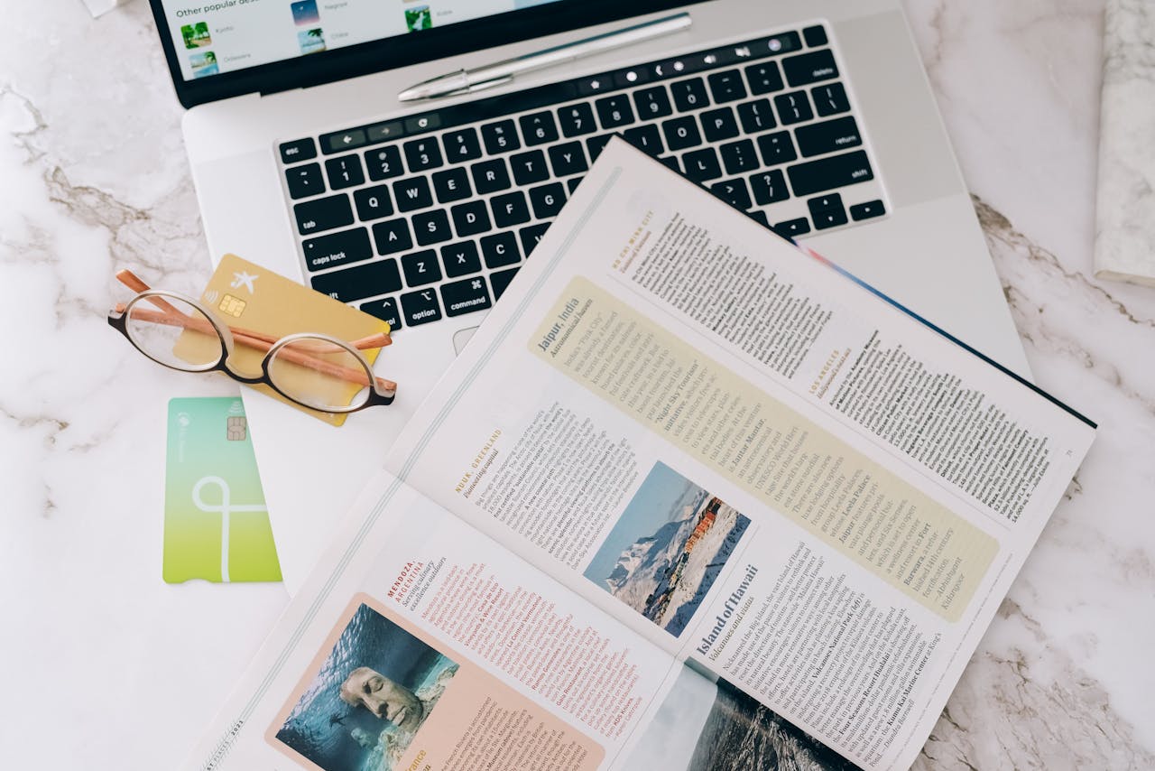 services-01 Flat lay image featuring a laptop, open magazine, credit cards, and eyeglasses on a marble table.